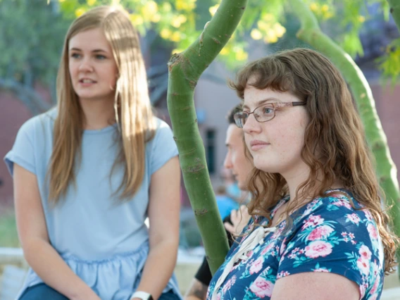 Three college students sitting outside listening to a friend.