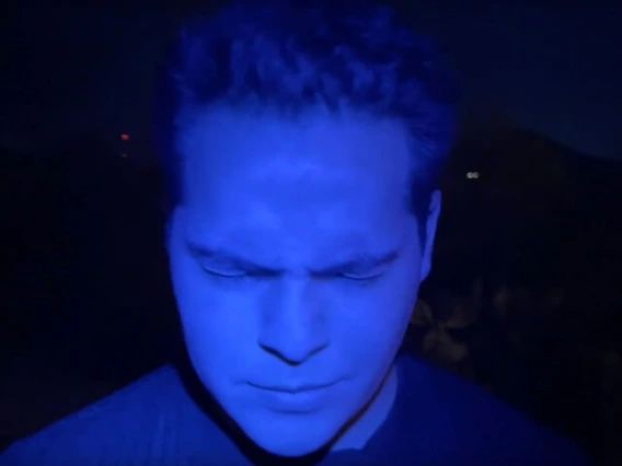 Man's face, looking down, washed in blue light