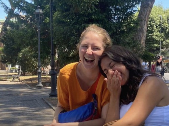 Two students laughing sitting on a bench in Italian piazza