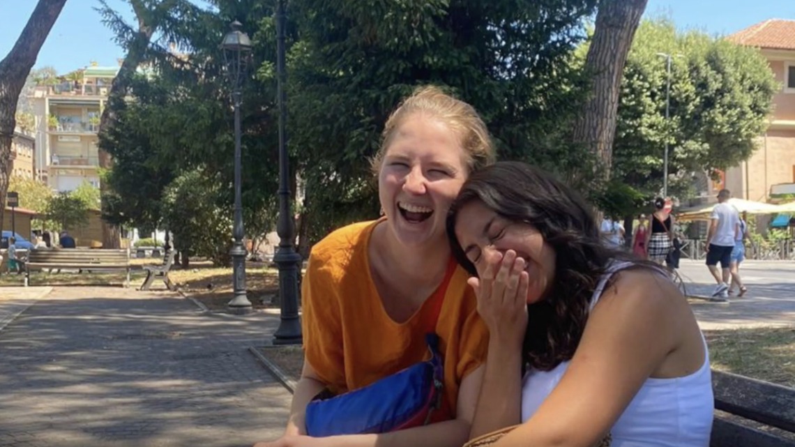 Two students laughing sitting on a bench in Italian piazza